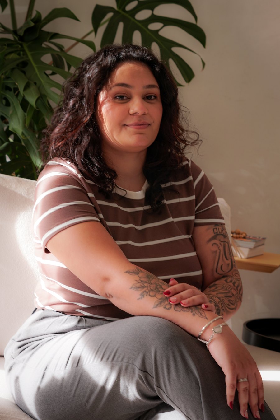 Yasmin Ribeiro, fundadora da Bloom Co., sentada em um sofá claro ao lado de uma planta.